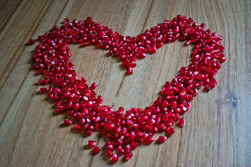 Pomegranate seeds shaped like a heart on a wooden table