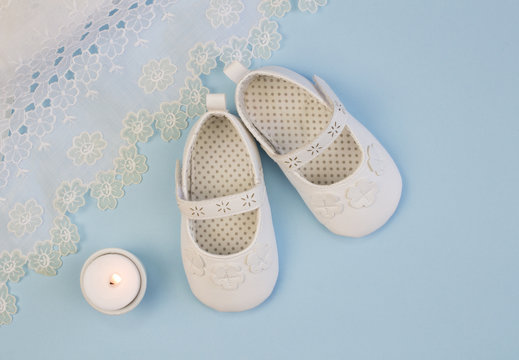 Pair of white baby booties on blue background with lace dress 