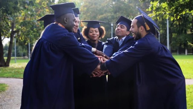 happy students in mortar boards with hands on top