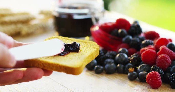 the hand of a young man in the morning for breakfast spreads of jam organic red fruits on a rusk . concept of organic jams and genuine and natural breakfast . Breakfast in the happy family