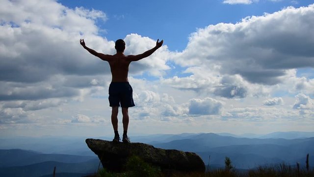 man stands on top of a mountain with open hands. 
