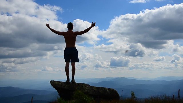 man stands on top of a mountain with open hands. 