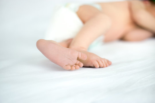 Close up of tiny sweet feet of sleeping newborn kid lying on white bed. Concept image