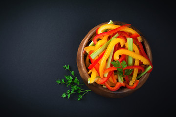 Celery, red and yellow pepper paprika vegetarian salad in a bamboo bowl on a dark background.Top view. Space for text. Selective focus.