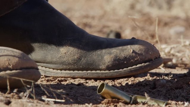 Four Bullet Shells Falling on the Dirt by a Mans Boot