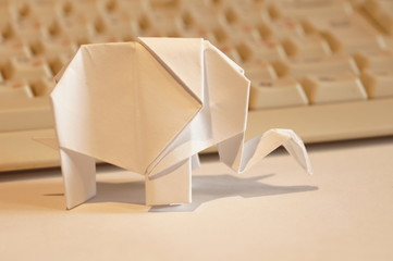 Paper origami elephant isolated on white background on the table next to the computer keyboard