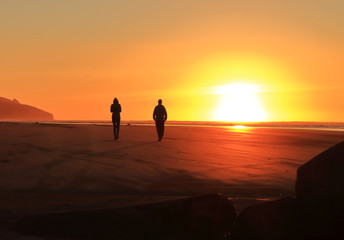 Fototapeta premium two people walking into sunset at beach