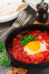 Shakshuka with tomato sauce and fried egg in a cast iron pan for breakfast on the old wooden background. Rustic Style, Selective Focus.