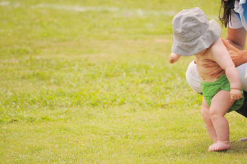 Little Toddler try to walk by his mom on grass field