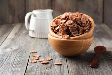 Chocolate cornflakes for breakfast in a bamboo plate on old wooden background. Selective focus.