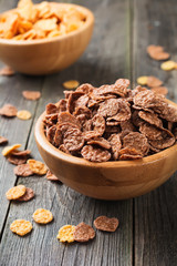 Chocolate cornflakes for breakfast in a bamboo plate on old wooden background. Selective focus.