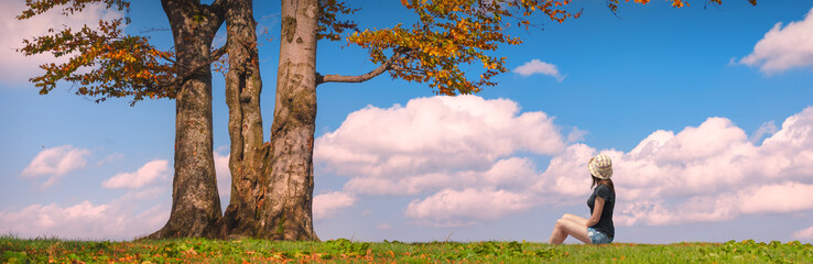 Woman sitting under the tree on a green hill