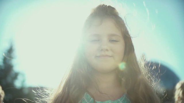 Portrait of cute little girl with chubby cheeks. Girl 7-9 years old smiling and says something. Girl with long hair in the sun. The girl says: "One, two, three, stand still!". Plump cheeks