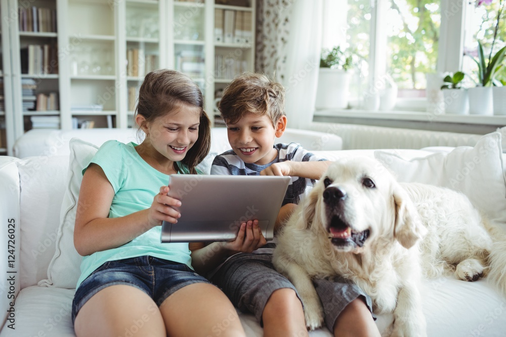 Poster children using digital tablet while sitting on a sofa