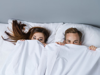 Playfull couple peeping from bedsheet