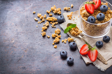 Homemade muesli granola in glass with berries on rusty table