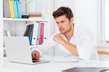 Handsome businessman sitting at the desk and using laptop