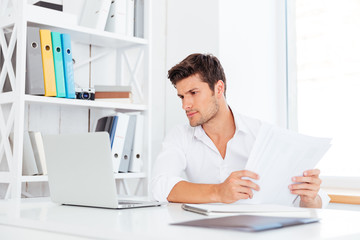 Naklejka premium Handsome young businessman working with documents and laptop
