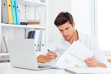 Obraz premium Concentrated young businessman sitting and writing at the table