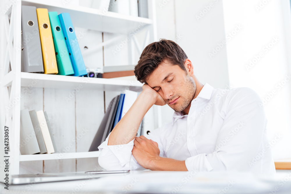 Wall mural young tired businessman sleeping at workplace