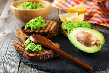 Sandwiches with guacamole traditional Mexican sauce, avocado and lemon on old wooden background. Selective focus.