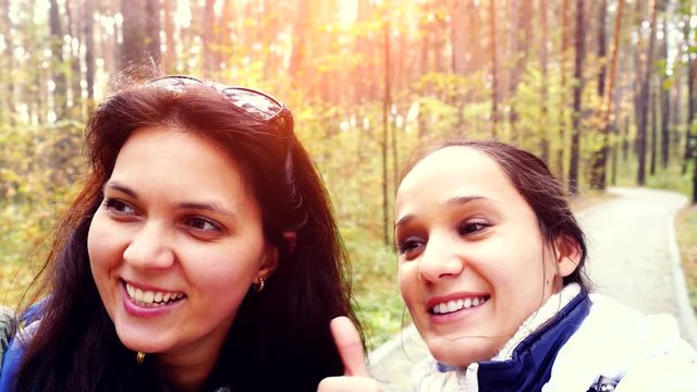 Two beautiful friends with cell phone camera taking photos selfie in autumn fall park. 3840x2160