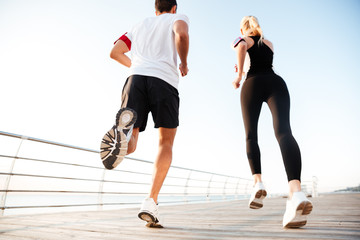 Back view of a young couple jogging at beach pier