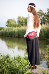 Portrait of young hippie lady with handbag standing by the lake