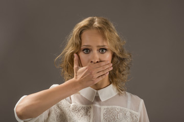 Pretty woman covering her mouth over gray background. Human emotion face expression. Stop talking!