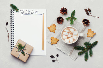 Cup of hot cocoa or chocolate with marshmallow, cookies and notebook with christmas to do list on white table from above. Traditional winter drink. Flat lay.
