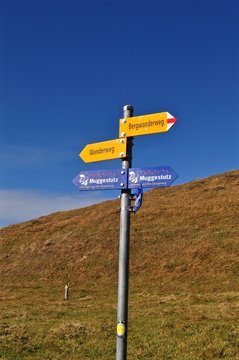 Gelber Wegweiser f&uuml;r Wanderer am Wanderweg in den Schweizer Alpen vor blauem Himmel