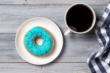Blue donut decorated with sprinkles and cup of coffee, wooden background