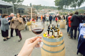 Glass of wine at tasting area of annual city festival Tbilisoba with crowd of people around....