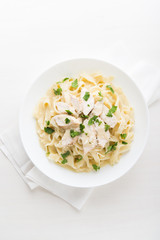 Pasta fettuccine alfredo with chicken, parmesan and parsley on white background top view. Italian cuisine.