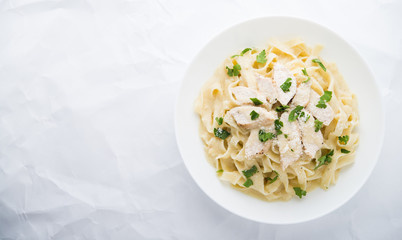 Pasta fettuccine alfredo with chicken, parmesan and parsley on white textured background top view. Italian cuisine. Space for text.
