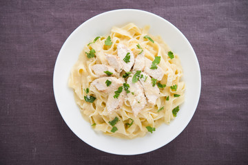 Pasta fettuccine alfredo with chicken, parmesan and parsley on dark background top view. Italian cuisine.