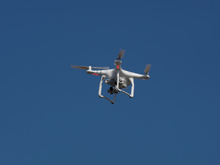 Underneath bottom view of a drone with stabilizer camera flying aerial overhead against a blue sky