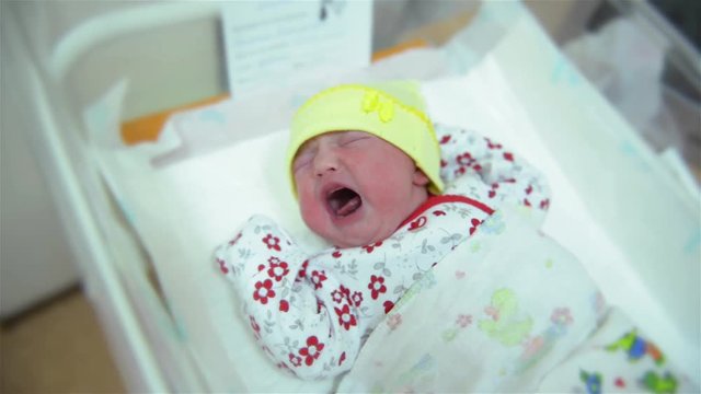 New born infant asleep in the blanket in delivery room, baby girl crying immediately after birth