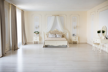 Bedroom in soft light colors. Big comfortable double bed in elegant classic interior