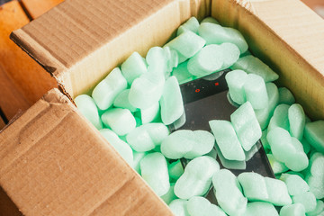 parcel of online shop, phone in a cardboard box on green styrofoam