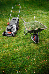 lawnmower and wheelbarrow with grass on mown green lawn