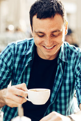 Fototapeta na wymiar Young man drinking coffee in a sidewalk cafe