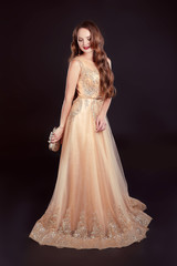 Fototapeta premium Attractive brunette woman in golden long dress isolated on black