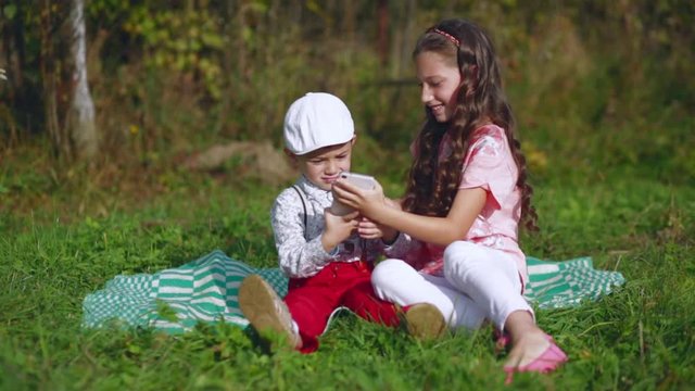 Little children play with a mobile phone in the garden