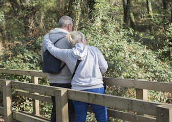 Fototapeta premium Mature couple standing on a bridge on a woodland area. 