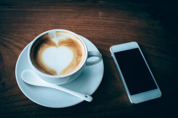 Fototapeta na wymiar mobile phone and coffee cup on wood table dark tone.