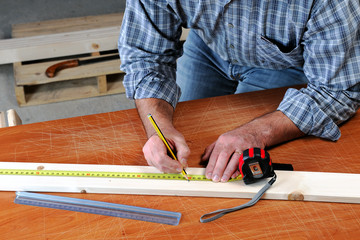 Artisan adult takes the measurement of a strip of wood to manufacture a product.