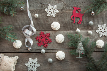 Christmas decor laid out on a wooden surface. Fir branches, silver ribbon and ball, white marshmallow, snowflakes, toy red deer and decor around. Top view and copyspace. Flat lay.