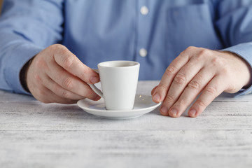 Man at table holds a cup of espresso coffee in his hand