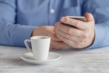Man sits with smartphone at table with cup of coffee